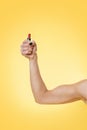 A woman`s strong arm shows off her biceps and holds a lipstick. Yellow background. Copy space. Feminism, girl power and the