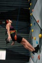 Woman in safety equipment and harness looking up while training on the artificial climbing wall indoors Royalty Free Stock Photo