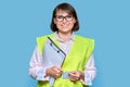 Woman in safety vest with fileholder looking at camera, light blue isolated background Royalty Free Stock Photo