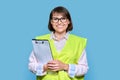 Woman in safety vest with fileholder looking at camera, light blue isolated background Royalty Free Stock Photo