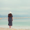 Woman in sailor striped dress near seaside of Dead Sea beach. Travel, summer vacation, holiday, freedom concept. Digital detox. Royalty Free Stock Photo