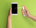 Woman sanitizing smartphone with antiseptic spray on green background. Be safety during coronavirus outbreak