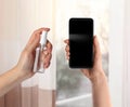 Woman sanitizing smartphone with antiseptic spray indoors. Be safety during coronavirus outbreak