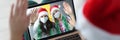 Woman in santa claus hat holds laptop on knees and communicates with her friends in protective masks
