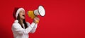 Woman In Santa Hat Making Xmas Announcement With Loudspeaker Over Red Background Royalty Free Stock Photo