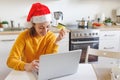 Woman in Santa hat shopping online and paying with gold credit card. Young girl with laptop buying Christmas gift present on Royalty Free Stock Photo