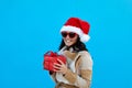 Woman in santa hat and sunglasses with gift blue background Royalty Free Stock Photo