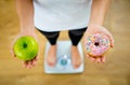 Woman on scale measuring weight holding apple and donuts choosing between healthy or unhealthy food Royalty Free Stock Photo