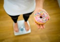 Woman on scale measuring weight holding apple and donuts choosing between healthy or unhealthy food Royalty Free Stock Photo