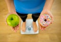 Woman on scale measuring weight holding apple and donuts choosing between healthy or unhealthy food Royalty Free Stock Photo