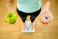 Woman on scale measuring weight holding apple and donuts choosing between healthy or unhealthy food Royalty Free Stock Photo