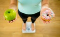 Woman on scale measuring weight holding apple and donuts choosing between healthy or unhealthy food Royalty Free Stock Photo