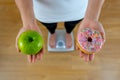 Woman on scale measuring weight holding apple and donuts choosing between healthy or unhealthy food Royalty Free Stock Photo