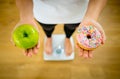 Woman on scale measuring weight holding apple and donuts choosing between healthy or unhealthy food Royalty Free Stock Photo