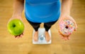 Woman on scale measuring weight holding apple and donuts choosing between healthy or unhealthy food Royalty Free Stock Photo