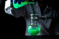 A woman scientist experimenting with a green fluorescent solution in a glass round bottom flask in dark chemistry laboratory Royalty Free Stock Photo