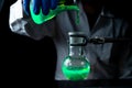 A woman scientist experimenting with a green fluorescent solution in a glass round bottom flask in dark chemistry laboratory Royalty Free Stock Photo