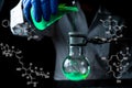 A woman scientist experimenting with a green fluorescent solution in a glass round bottom flask in dark chemistry laboratory Royalty Free Stock Photo