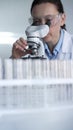 Woman scientist wearing lab coat and protective glasses is using microscope in modern laboratory setup. Low key lighting Royalty Free Stock Photo