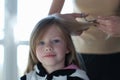 Woman scissors hair of cute blonde little girl closeup