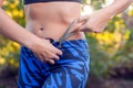 Woman with scissors trying to cut fat from her body outdoor. Slimming and diet concept