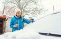 Woman scraping off ice from front window of her car in winter