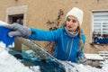 Woman scraping off ice from front window of her car in winter