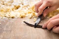 Woman scraping vanilla pulp from inside bean, cookie or cake dough in the background