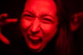 Woman screaming close-up to camera in red neon light, furious face, hysterics