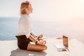 Woman sea laptop yoga. Business woman freelancer in yoga pose working over blue sea beach at laptop and meditates. Girl Royalty Free Stock Photo