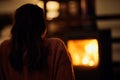 Woman seated in a cozy living space with a warm fire crackling in the background.