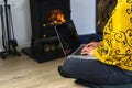 Woman seated on the floor working on her laptop computer in front of a wood burning stove or fireplace. Royalty Free Stock Photo