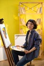 A woman seems very focused on her work as she is painting something on a canvas and wearing a blue flannel shirt with