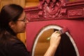 Woman with serious facial expression aging carved ornaments of antique wooden cupboard door in pink color. Giving new