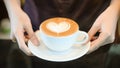 Woman serving coffee while standing in coffee shop. Focus on Latte art hearth shape cup in female hands while placing of coffee on