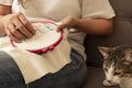 Woman sewing cross stitch with her cats on the sofa at home