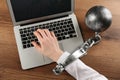 Woman shackled with ball and chain typing on laptop at wooden table, above view. Internet addiction