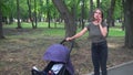 Woman shakes baby in stroller outdoors and talking on smartphone Royalty Free Stock Photo