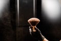 A woman shakes a large powder brush with clouds of dust on a black background. Treatment after instant tanning Royalty Free Stock Photo