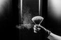 A woman shakes a large powder brush with clouds of dust on a black background. Treatment after instant tanning Royalty Free Stock Photo