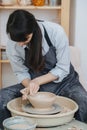 Woman shaping clay bowl on a pottery wheel in her private workshop