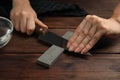 Woman sharpening knife at wooden table, closeup