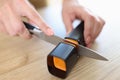 Woman sharpens knife with sharpener in kitchen close-up.