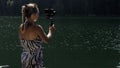 Woman shooting on handheld film gimbal stabilization for smartphone. Girl stand on pier make selfie. Blogger broadcast