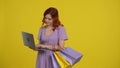 A woman with shopping bags is using a laptop, looking through great deals. Redhaired woman in a light sundress in the