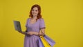 A woman with shopping bags is using a laptop, looking through great deals. Redhaired woman in a light sundress in the