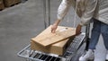 Young woman with shopping cart walking for choosing new furniture in big store warehouse and put some boxes in trolley