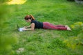 Woman is shopping on a laptop while lying on her stomach on green grass in a park. A student with two glasses is