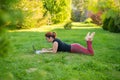 Woman is shopping on a laptop while lying on her stomach on green grass in a park. A student with two glasses is