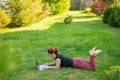 Woman is shopping on a laptop while lying on her stomach on green grass in a park. A student with two glasses is